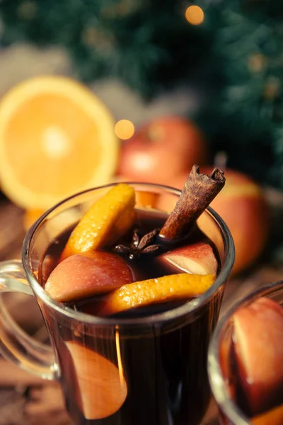Κοντινό πλάνο, Χριστουγεννιάτικο ζεστό κρασί με φρούτα και μπαχαρικά σε ξύλινο τραπέζι. Χριστούγεννα διακοσμήσεις στο παρασκήνιο. Χειμώνα του πλανήτη ποτό με φρούτα συστατικά γύρω από. — Φωτογραφία Αρχείου