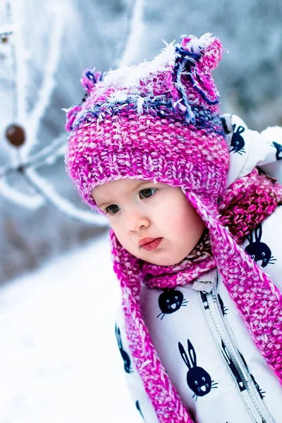 Enfant par temps neigeux. Bébé fille en blanc snowsuite et chapeau rose, bottes gants dans le parc d'hiver de neige . — Photo