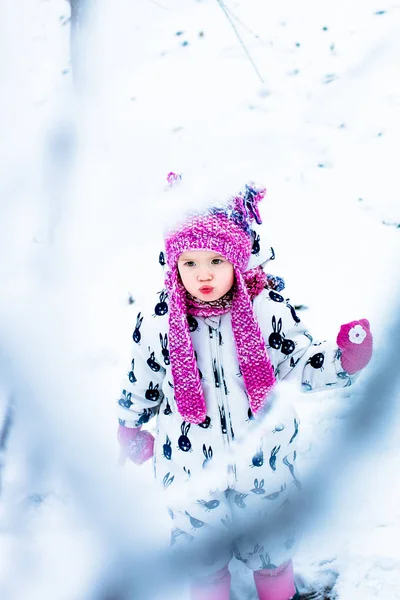 Bambino in giorno nevoso. Bambina in snowsuite bianca e cappello rosa, guanti da stivali nel parco neve invernale . — Foto Stock