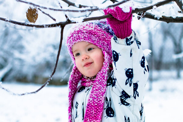 Ребенок в снежный день. Девочка в белом сноуборде и розовой шапке, сапоги в снежном зимнем парке
.  