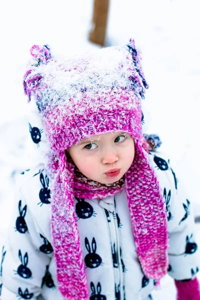Bambino in giorno nevoso. Bambina in snowsuite bianca e cappello rosa, guanti da stivali nel parco neve invernale . — Foto Stock