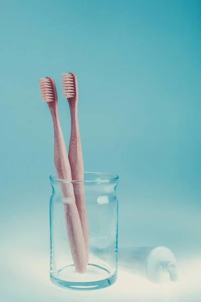 Két bézs fogászati kefék-üveg csésze áthallatszott fogkrém kék fehér háttér. Elszigetelt. Tónusú fénykép. — Stock Fotó