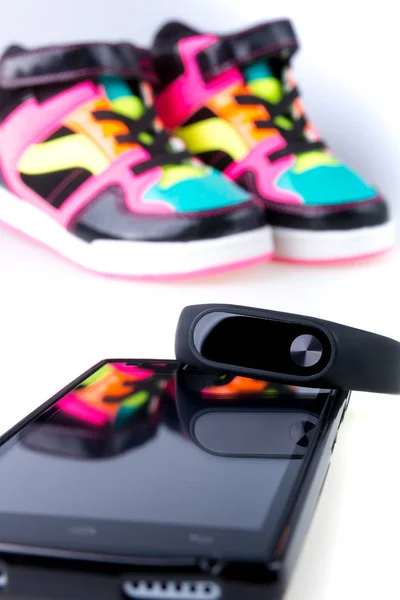 Pulsera de fitness y smartphone cerca de zapatillas deportivas multicolor. Aislado . — Foto de Stock