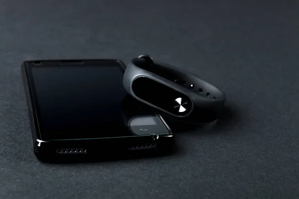 Pulsera deportiva y smartphone sobre fondo negro . — Foto de Stock