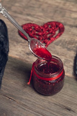 Ahududu reçeli bir kaşık kırmızı kalp yakınındaki kavanoza ahşap arka plan üzerine dökülür. Seviyorum. Sevgililer günü. Üstten Görünüm.