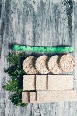 Teyp ve gri arka plan üzerinde yeşil roka ölçme yakınındaki crispbread parçaları. Diyet kavramı. Sağlıklı gıda. Üstten Görünüm. Uzay kopyalayın. Çerçeve.