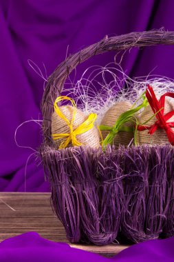 Paskalya yumurtası dekoratif mor sepette mor zemin üzerine ahşap masa üstünde sicim.