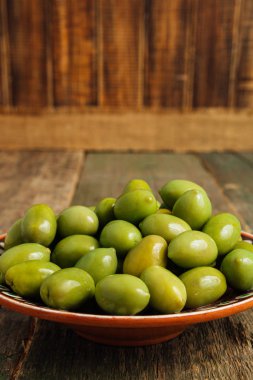 Yeşil zeytin ahşap arka plan üzerinde kahverengi kase. Yakın çekim.