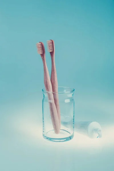 Két bézs fogászati kefék-üveg csésze áthallatszott fogkrém kék fehér háttér. Elszigetelt. Tónusú fénykép. — Stock Fotó