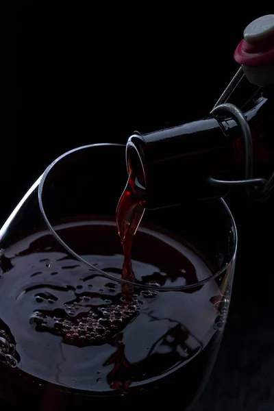 Pouring red wine from bottle into the wineglass on black background. — Stock Photo, Image