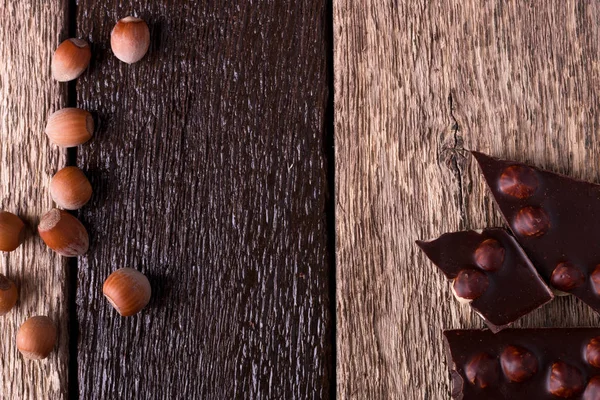 Chocoladestukjes met hazelnoot noten op houten achtergrond. Bovenaanzicht. Kopieer ruimte. Frame. — Stockfoto
