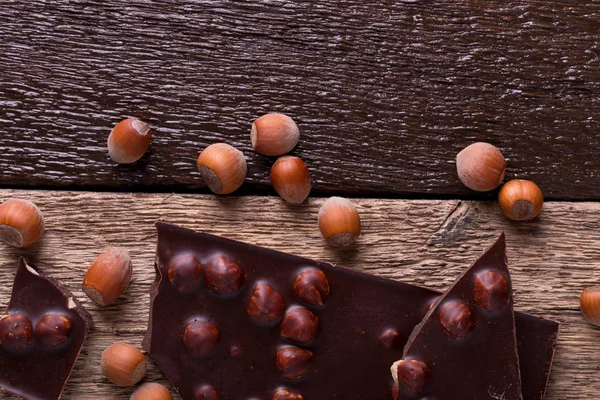 Chocoladestukjes met hazelnoot noten op houten achtergrond. Bovenaanzicht. Kopieer ruimte. Frame. — Stockfoto