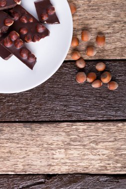 Beyaz tabak ahşap arka plan üzerinde Fındıklı Fındıklı çikolata parçaları. Üstten Görünüm. Uzay kopyalayın. Çerçeve.