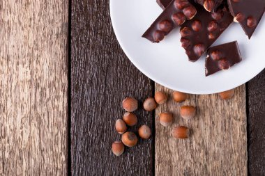 Beyaz tabak ahşap arka plan üzerinde Fındıklı Fındıklı çikolata parçaları. Üstten Görünüm. Uzay kopyalayın. Çerçeve.