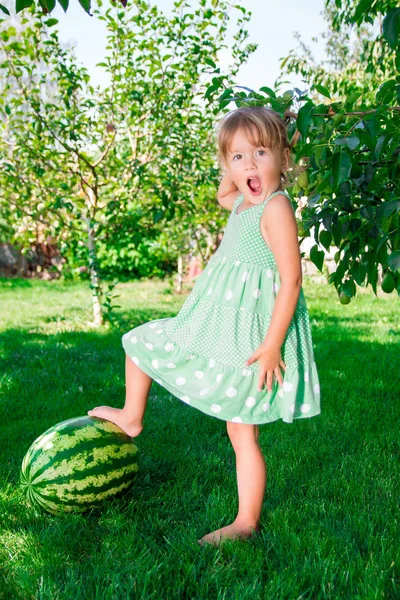 Bambina in abito verde a piedi nudi in piedi su anguria — Foto Stock