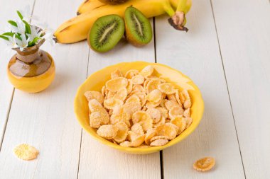 Tahıl gevreği ve beyaz zemin üzerine çiçekli vazo yakın meyve sağlıklı kahvaltı. Sarı tonu.