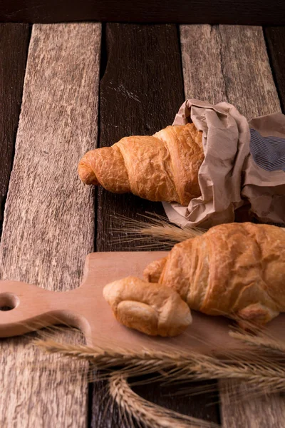 Croissants on board near wheat on wooden sackcloth background. Rustic style. — Stock Photo, Image