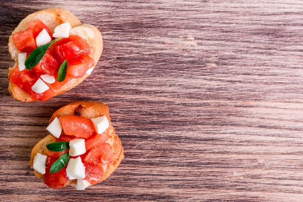Bruschetta s rajčaty, mozzarellou a bazalkou na dřevěné pozadí. Pohled shora. Kopírovat prostor. — Stock fotografie