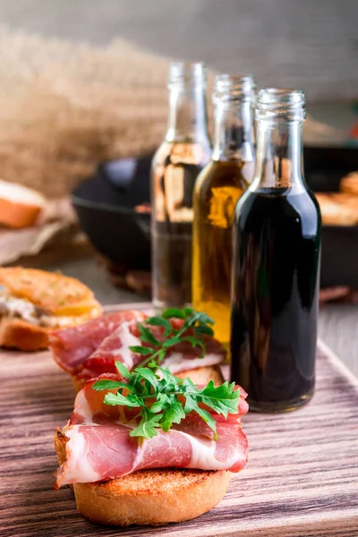 Bruschetta jambon ve ahşap zemin üzerine sosu şişesiyle yakınındaki roka ile — Stok fotoğraf