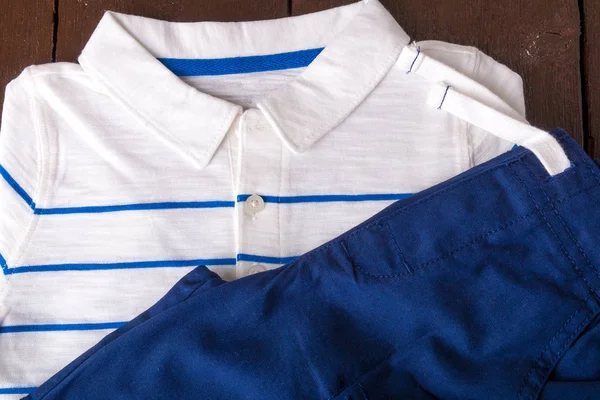 Kék nadrág és fehér csíkos póló, barna fa háttér. Fiú ruhát. Szemközti nézet. — Stock Fotó