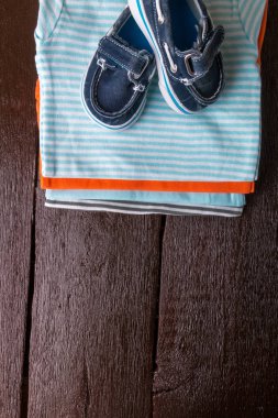 Tekne ayakkabı ile mavi ve turuncu gömlek üzerinde ahşap arka plan üzerinde katlanmış. Yeni doğan çocuk için bebek bezi. Bebek Giyim yığını. Çocuk kıyafeti. Üstten Görünüm.