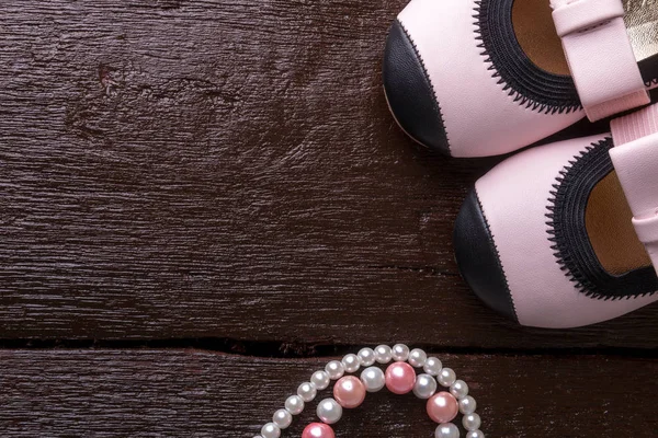 宝贝女孩粉红色鞋子附近木制背景上的珍珠。顶视图 — 图库照片