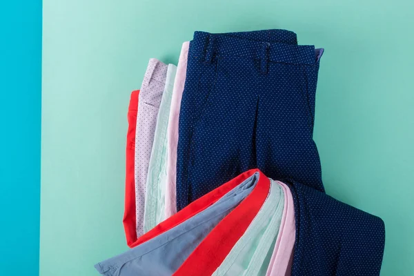 Gevouwen kleurrijke broeken en jeans op mint achtergrond. Bovenaanzicht. — Stockfoto