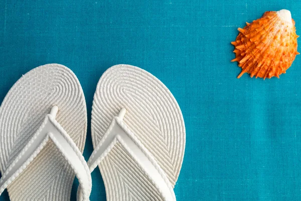 White flip flop near seashell on blue background. Top view. — Stock Photo, Image