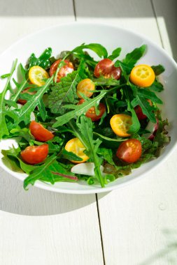 Beyaz ahşap zemin üzerinde Kamkat ve domates kiraz ile taze Roka Salatası. Üstten Görünüm. Sağlıklı gıda. Diyet.