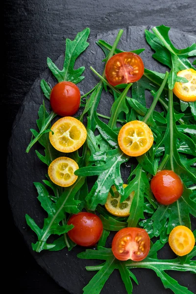 Vegetarischer Rucolasalat mit Kumquat und Tomatenkirsche auf Schieferteller. Ansicht von oben. Gesunde Ernährung. Ernährung. — Stockfoto