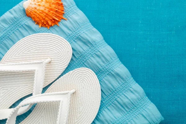 White flip flop near seashell on blue background. Top view. — Stock Photo, Image