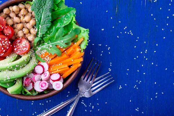 Veganská buddha mísa na modré dřevěné pozadí. Mísa s mrkev, salát, cherry rajčata, ředkev, avokádo a cizrna. Vegetariánská, zdravá, detoxikační potraviny koncept. Pohled shora. — Stock fotografie