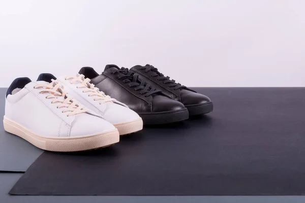 Dva páry bot tenisky na černém pozadí. Černá a bílá obuv. — Stock fotografie