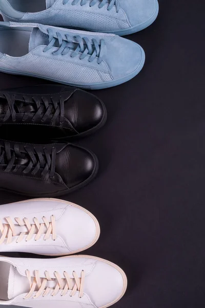 Tres zapatillas de deporte sobre fondo negro. Zapato negro, blanco y azul. Vista superior. Copiar espacio . —  Fotos de Stock