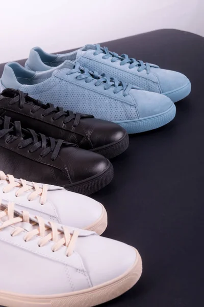 Tre par sneakers på svart bakgrund. Svart, vit och blå sko. — Stockfoto