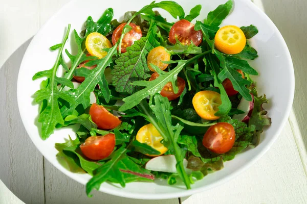 Frischer Rucolasalat mit Kumquat und Tomatenkirsche auf weißem Holzgrund. Ansicht von oben. Gesunde Ernährung. Ernährung. — Stockfoto