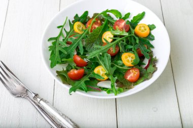 Beyaz ahşap zemin üzerinde Kamkat ve domates kiraz ile taze Roka Salatası. Üstten Görünüm. Sağlıklı gıda. Diyet.