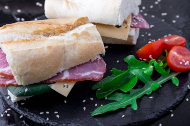 Jamon, roka, domates, peynir taş kayrak siyah arka plan üzerine ile sandviç. Yakın çekim