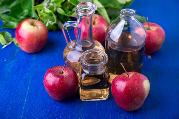 Apfelessig. drei Glasflaschen auf blauem Hintergrund. rote Äpfel. — Stockfoto