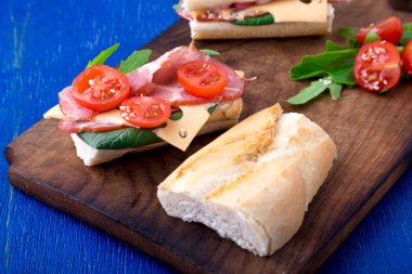 Jamon, roka, domates, peynir ahşap Pano mavi zemin üzerine açık sandviç. Rustik.