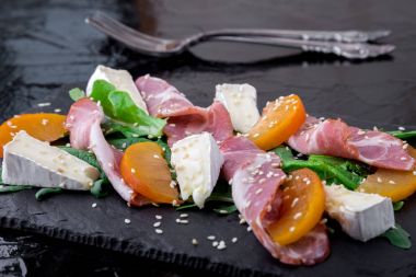 Salata ile ham jamon serrano, camembert, roka, siyah arka plan üzerine siyah taş kayrak tabakta kavun. Yakın çekim