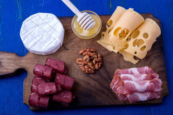 Сир і м'ясна тарілка з волоськими горіхами на синьому дерев'яному фоні. Вид зверху . — стокове фото
