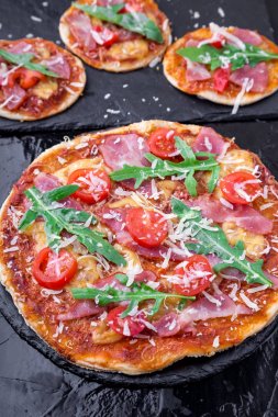 Ev yapımı pizza salam, domates, roka siyah arduvaz gemide. Yakın çekim.