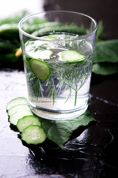 Cucumber water in glass with dill on black background. Detox, diet. Backlight.