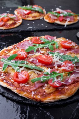 Ev yapımı pizza salam, domates, roka siyah arduvaz gemide. Yakın çekim.