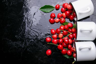 Dağınık kiraz emaye bardak dan. Kiraz demir Kupası siyah arka plan üzerine. Sağlıklı, yaz meyve. Kiraz. Üç. Üstten Görünüm.