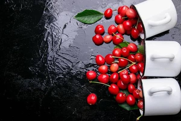 Dağınık kiraz emaye bardak dan. Kiraz demir Kupası siyah arka plan üzerine. Sağlıklı, yaz meyve. Kiraz. Üç. Üstten Görünüm.