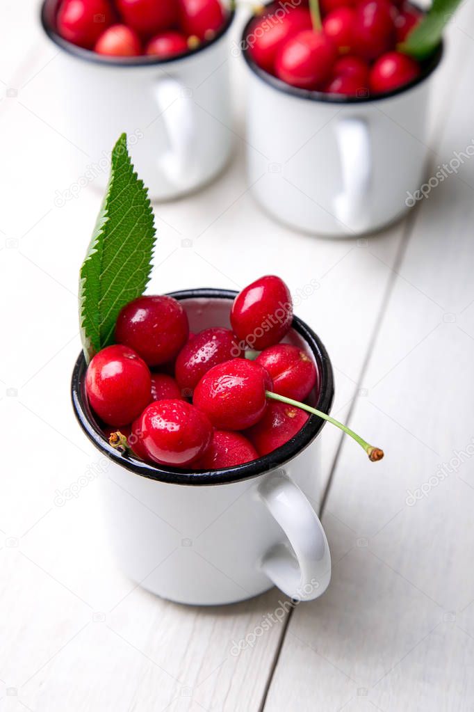 Cherry in enamel cup on white wooden background. Healthy, summer fruit. Cherries