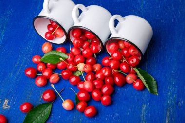 Dağınık kiraz emaye bardak dan. Kiraz demir Kupası mavi ahşap zemin üzerinde. Sağlıklı, yaz meyve. Kiraz. Üç. Yakın çekim.