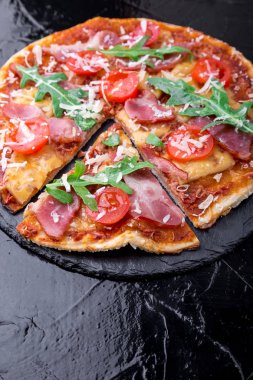 Ev yapımı pizza salam, domates, roka siyah arduvaz gemide. Yakın çekim.